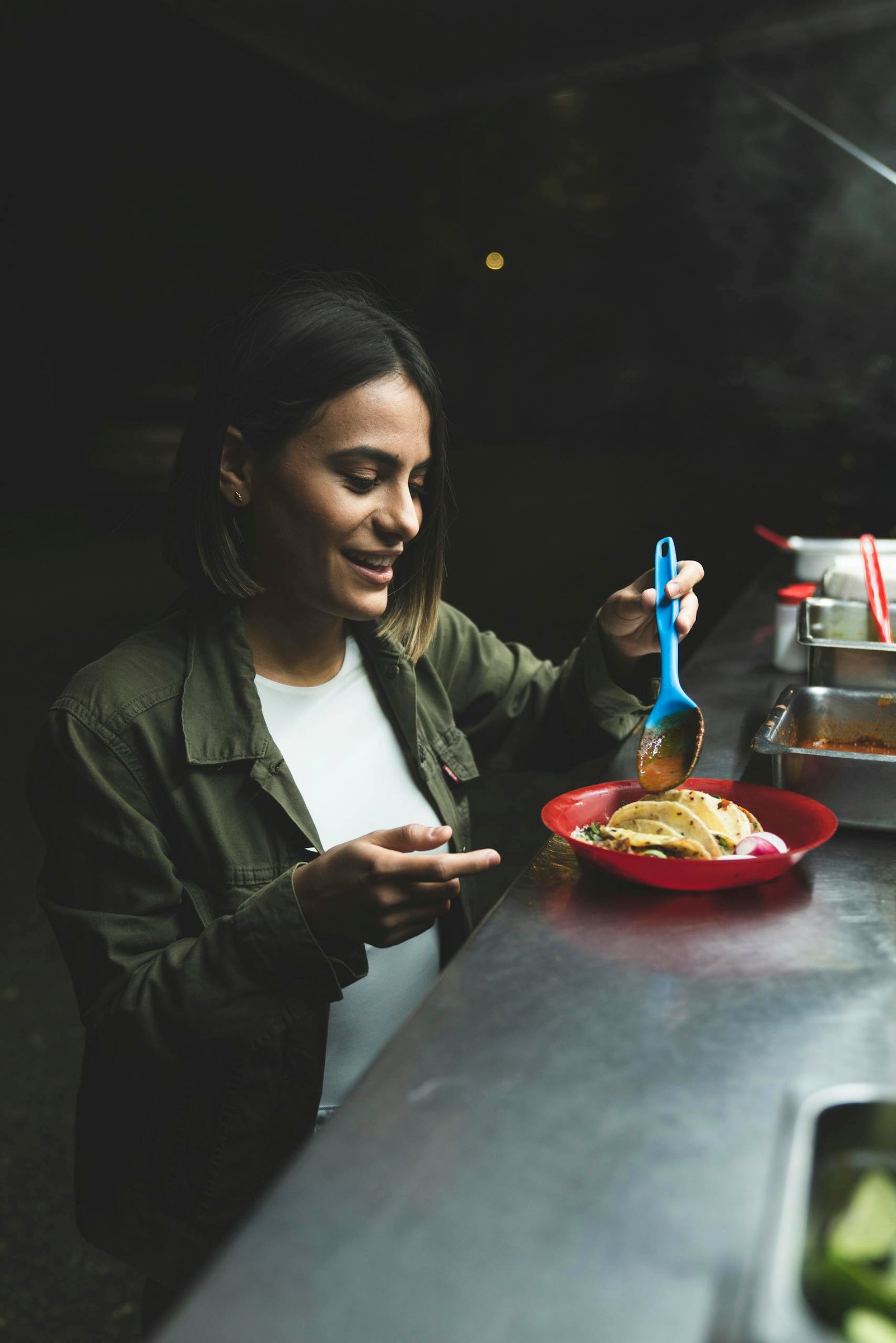 A woman eating tacos at a street food stand, vividly captured outdoors at night.